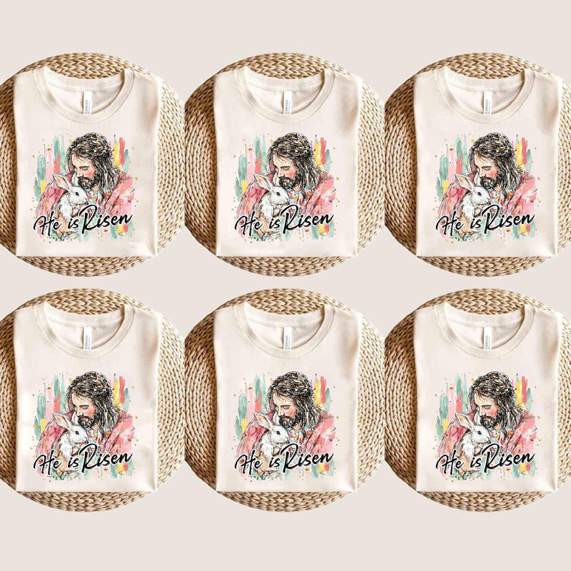 Christliches Oster T-Shirt „He Is Risen“ – Jesus hält ein weißes Häschen im …